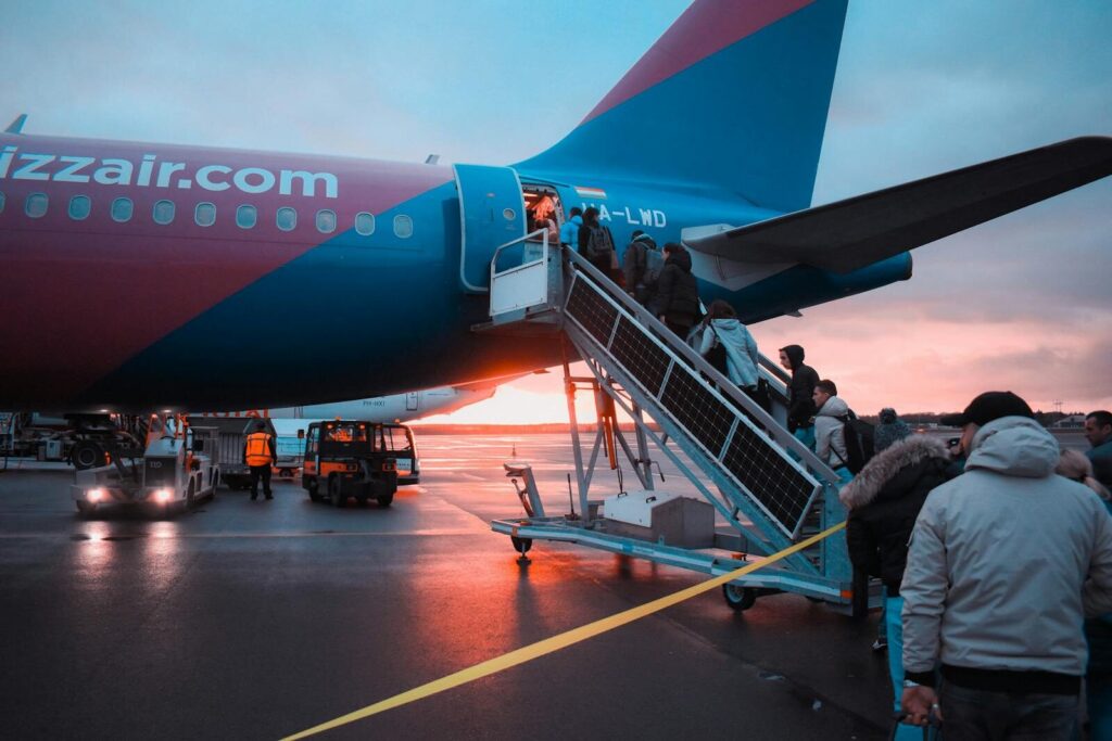 Passagerer går ombord på et fly i en mindre lufthavn med solnedgang i baggrunden